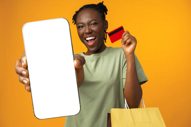 Smiling young afro girl holds smart phone and credit card in yellow studio, close up